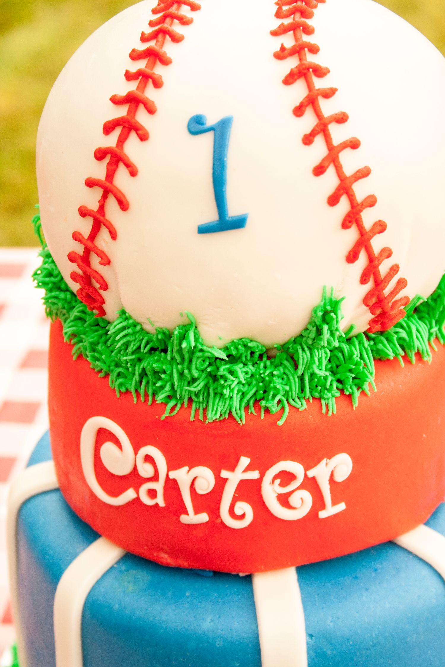 Close-up of baseball themed cake top tier with number 1 and red stitching design.