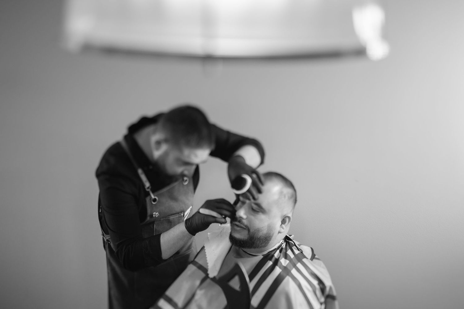 Black and white photo of barber giving precise haircut in professional setting.