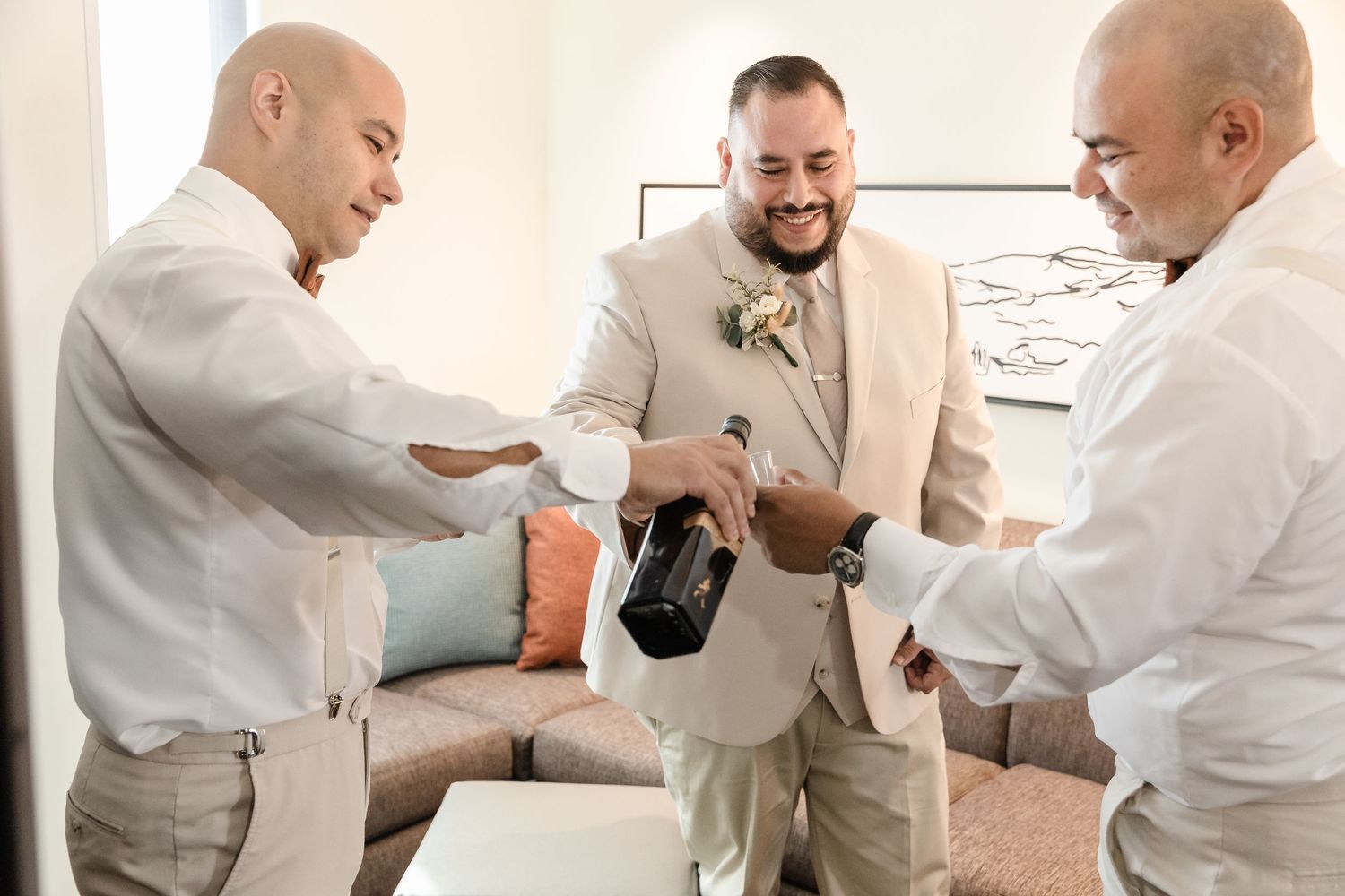 Group in formal white attire sharing drinks and laughs during pre-event gathering.