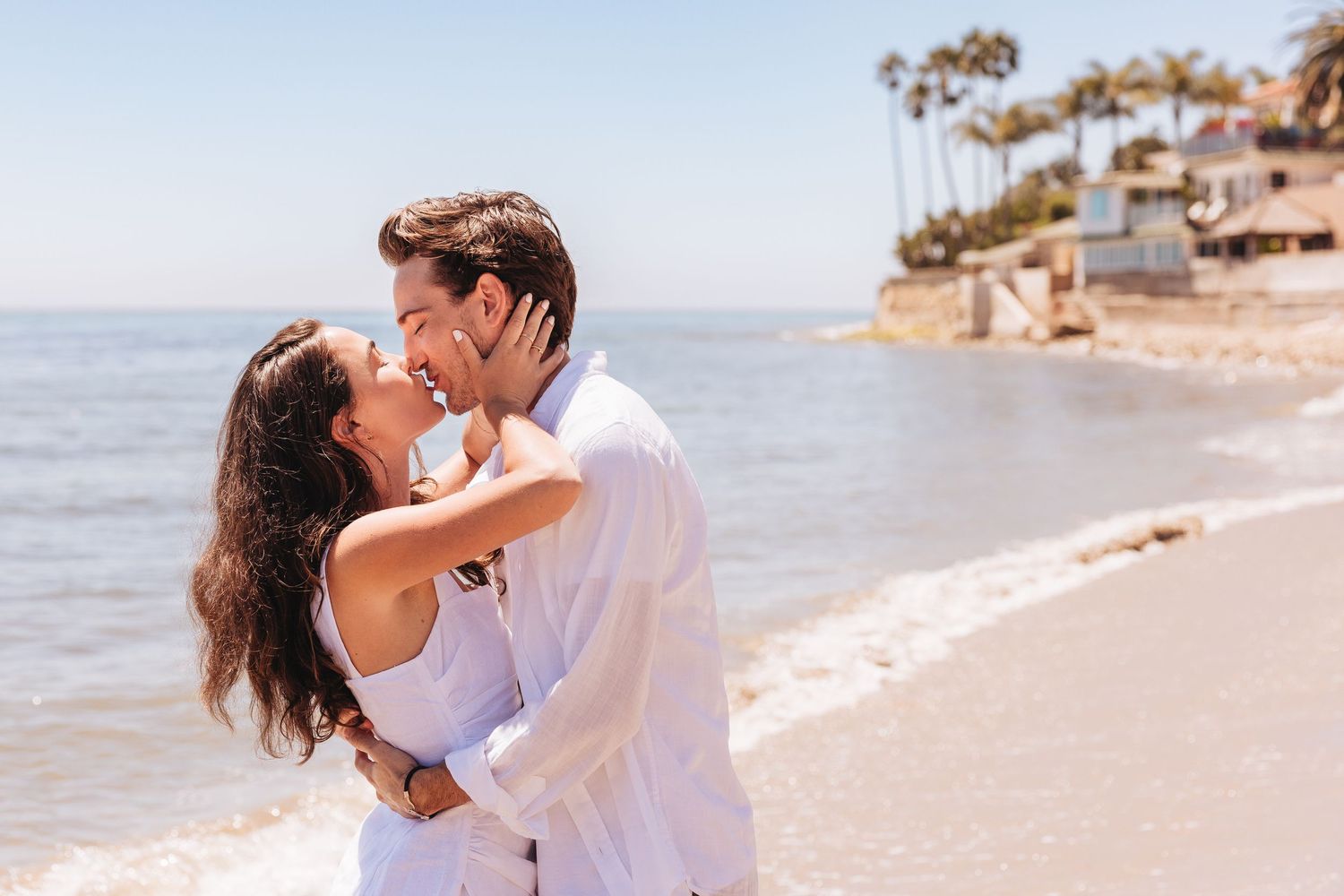 Romantic couple embracing on a sunny beach with ocean waves in the background.