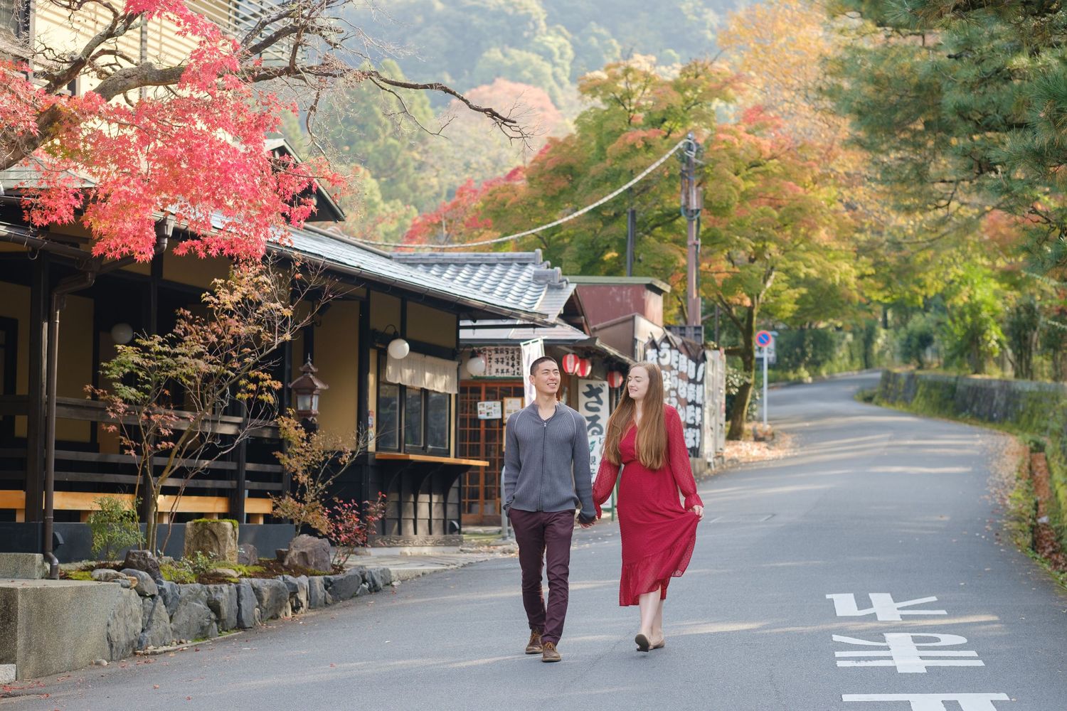 Couple walking hand in hand down a quiet Japanese street lined with traditional buildings in autumn.
