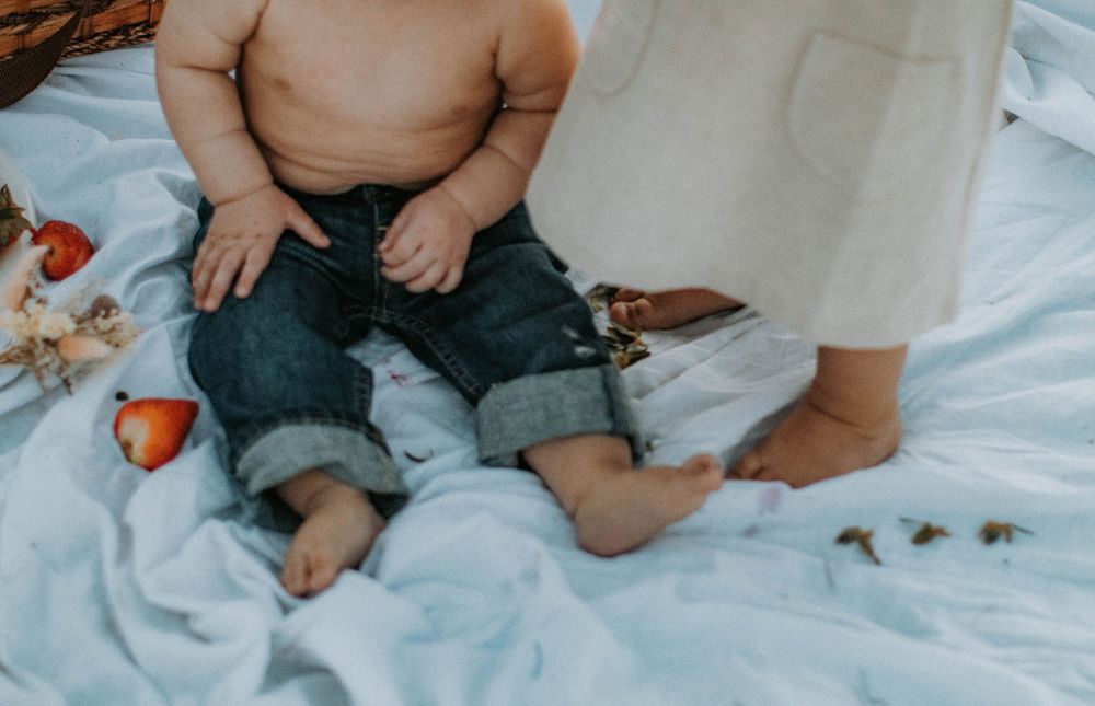 Baby sitting on white blanket playing with toys.