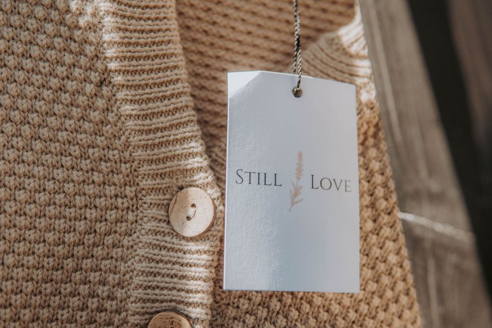 Close-up of beige knit sweaters with price tags hanging on retail display.