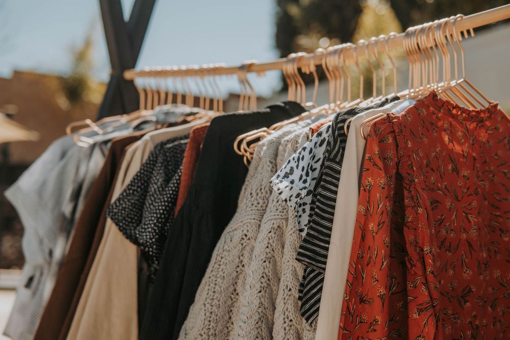 Clothing rack displaying various women's dresses and tops in earth tones and red lace.