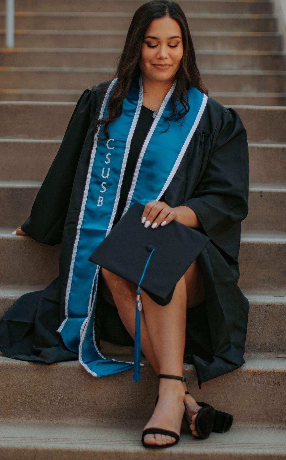 Graduation photos on stone steps featuring traditional black cap, gown and blue stole.