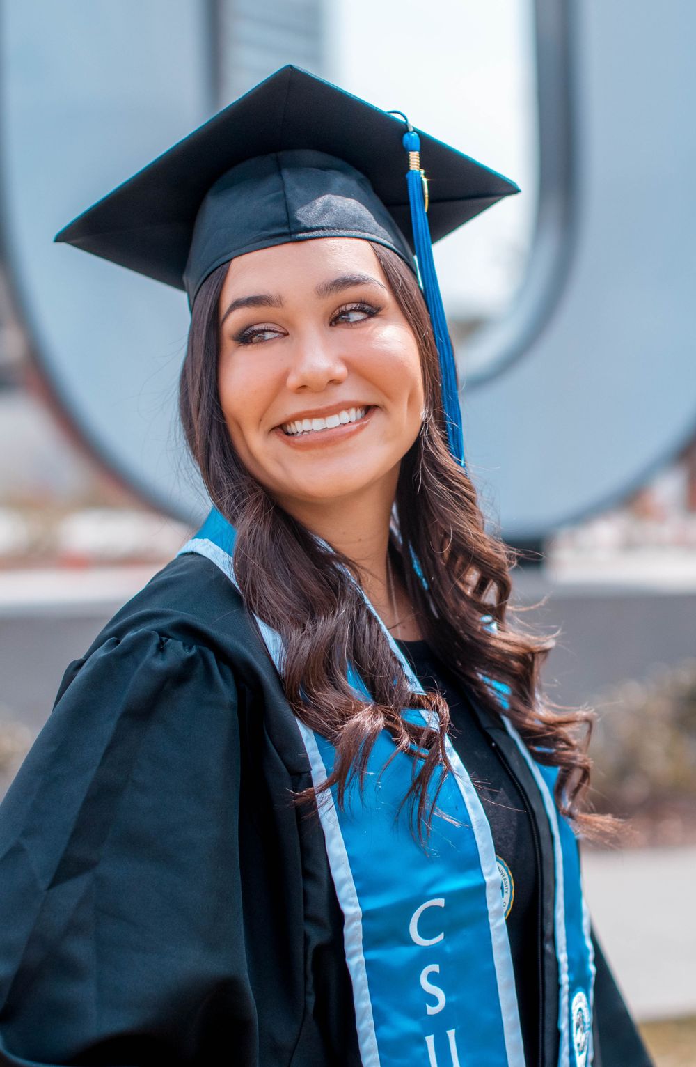 Graduate in cap and gown displaying a blue academic stole during outdoor commencement photoshoot.