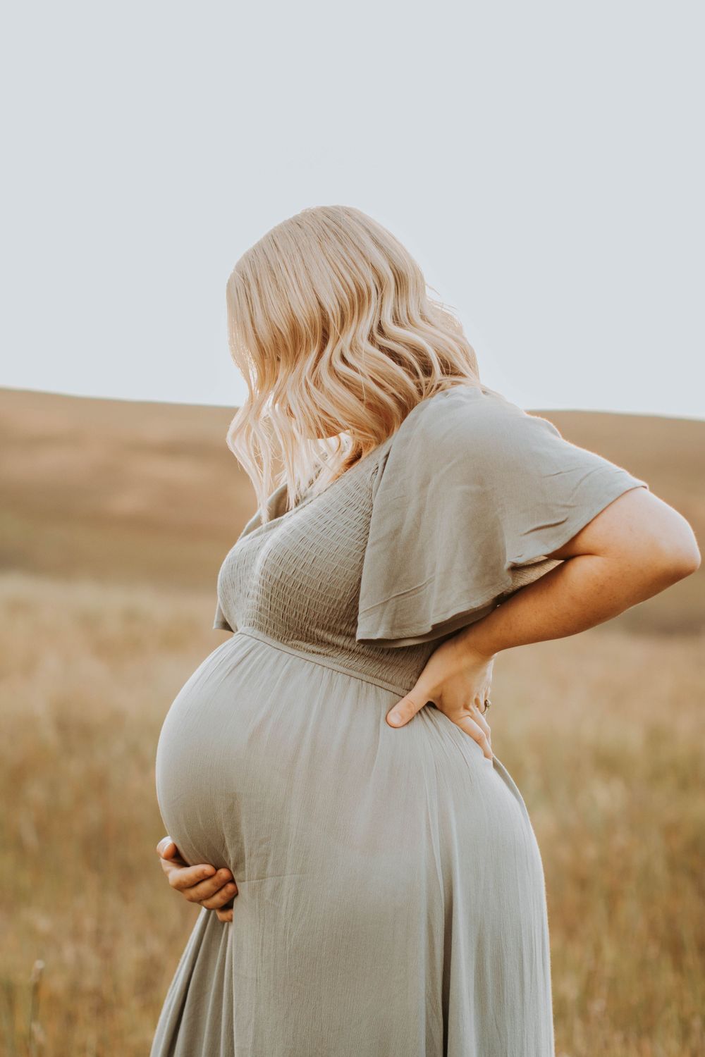Maternity portrait series showing gentle embrace of pregnant belly in warm sunlight.