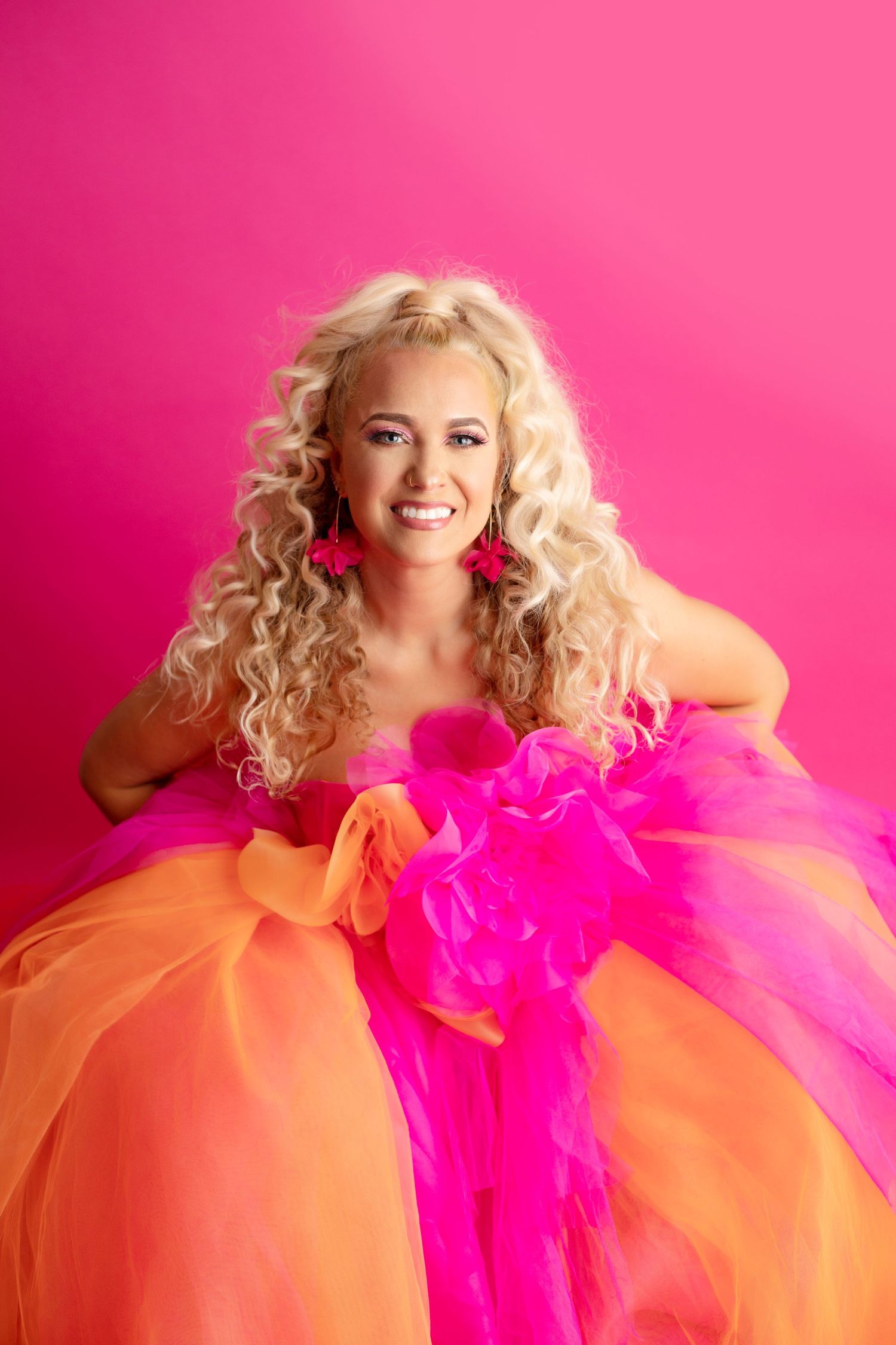 Joyful portrait in orange and pink tulle ballgown against bright pink background.