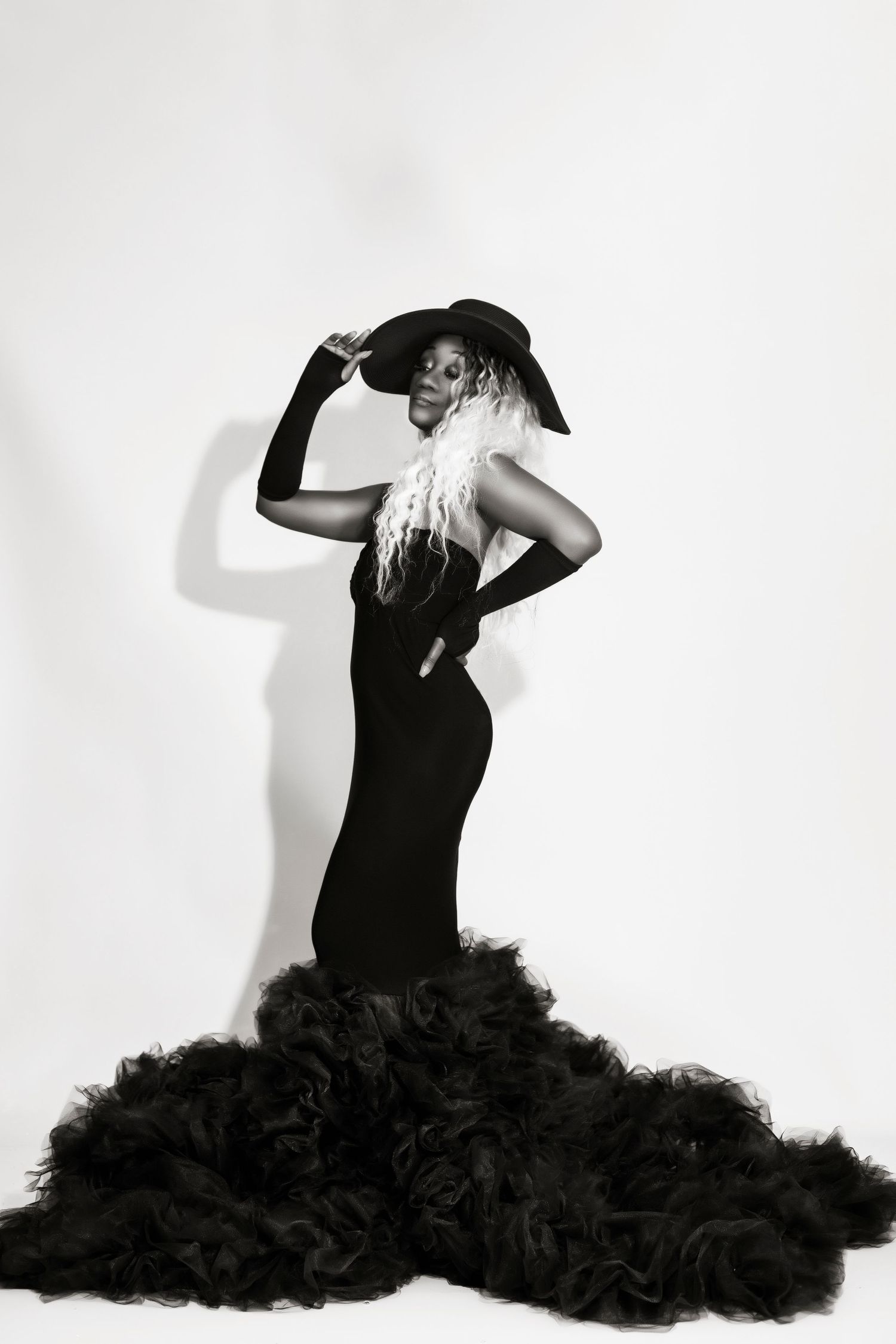 Dramatic black and white photo of flowing black gown with tulle train and wide-brimmed hat.