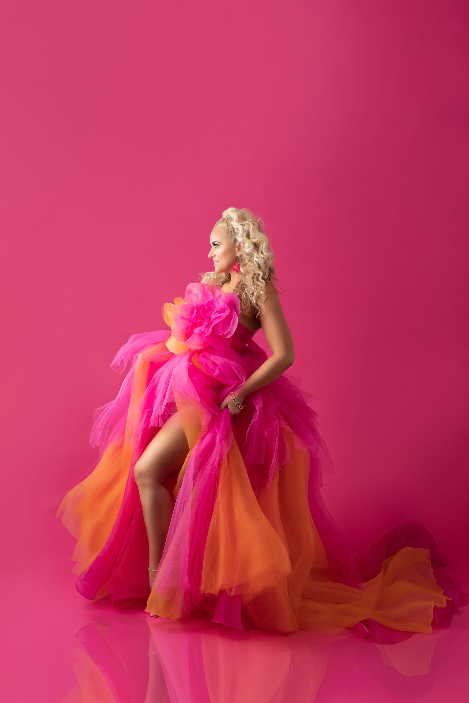 Dramatic fashion photo of flowing pink and orange tulle gown against vibrant pink backdrop.