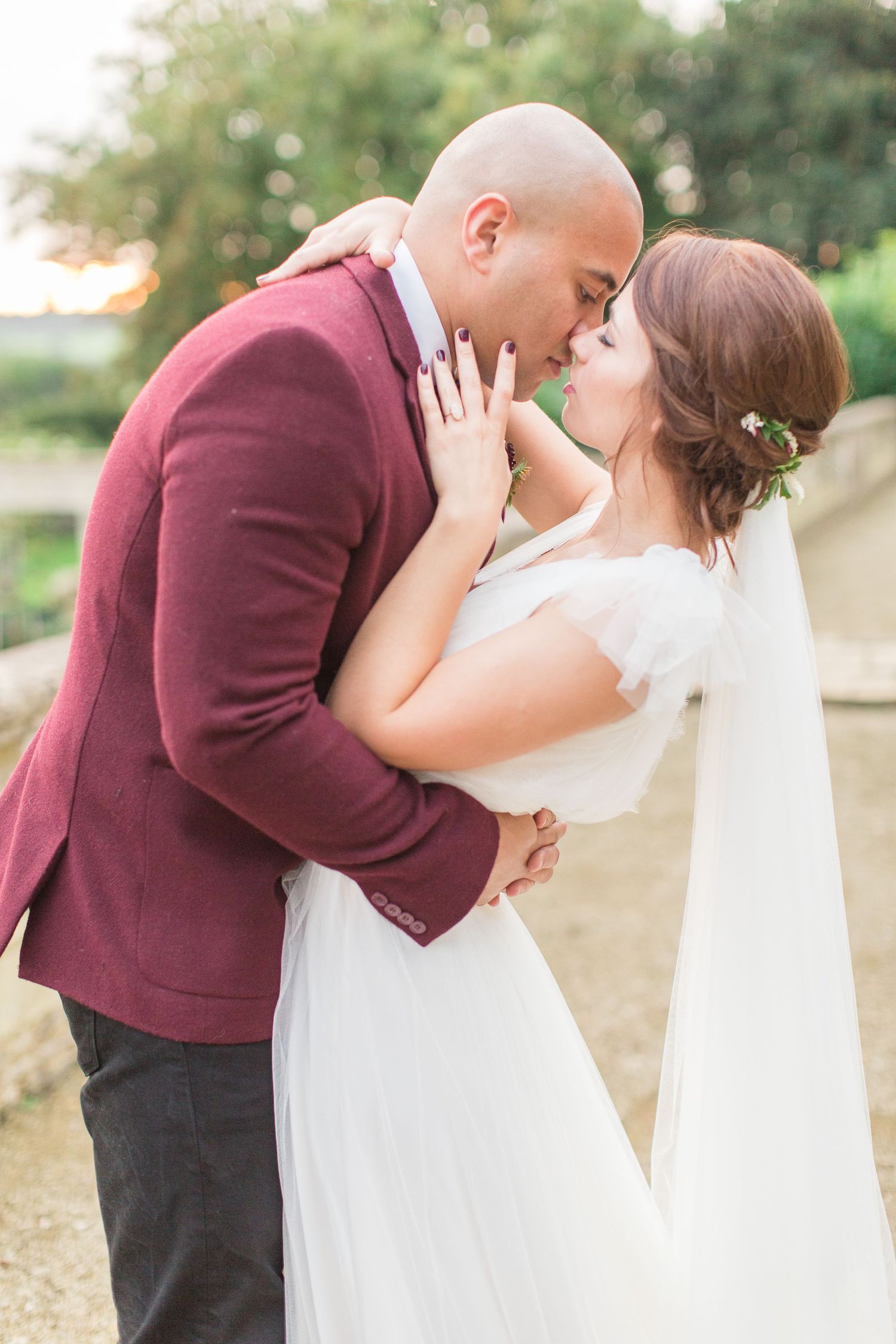 A romantic wedding couple share a tender kiss outdoors, with the bride in white and groom in burgundy jacket euridge manor