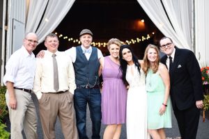 Group wedding photo of guests and wedding party outside barn venue with string lights.
