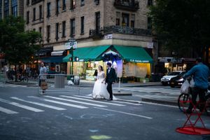 A couple crossing a New York City street in wedding attire while a cyclist passes by.