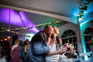 Wedding reception scene under tent with colorful uplighting and string lights.