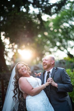 A joyful wedding moment captured in natural sunlight with bokeh effect through trees.