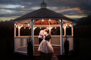 Romantic sunset wedding photo of couple in illuminated gazebo at twilight.