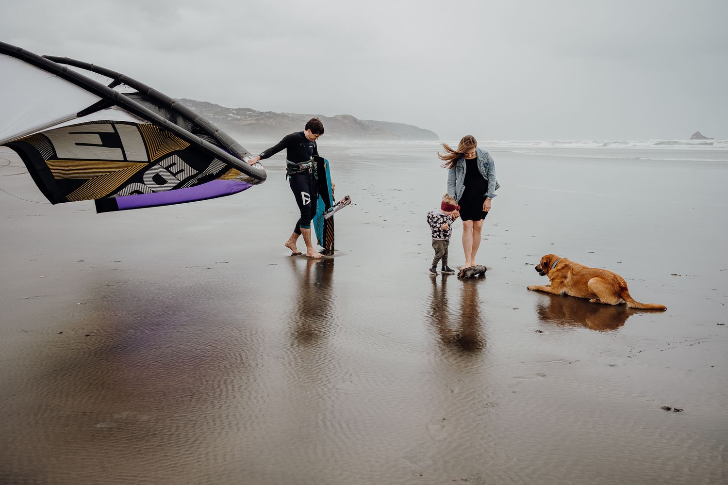 Dad's finished kite surfing, mum and her daughter are playing with the dog, this is real family life.
