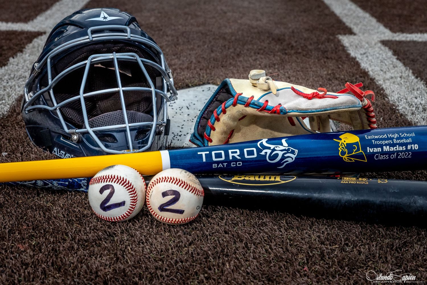 Baseball equipment including bats, helmets, and balls arranged on brown dirt field.
