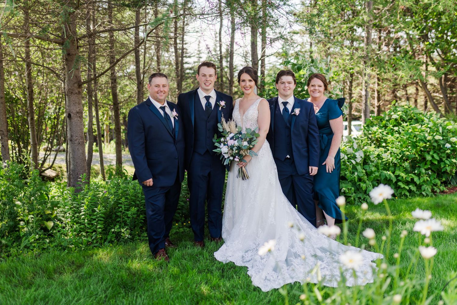Wedding party poses for formal photo in wooded garden setting.
