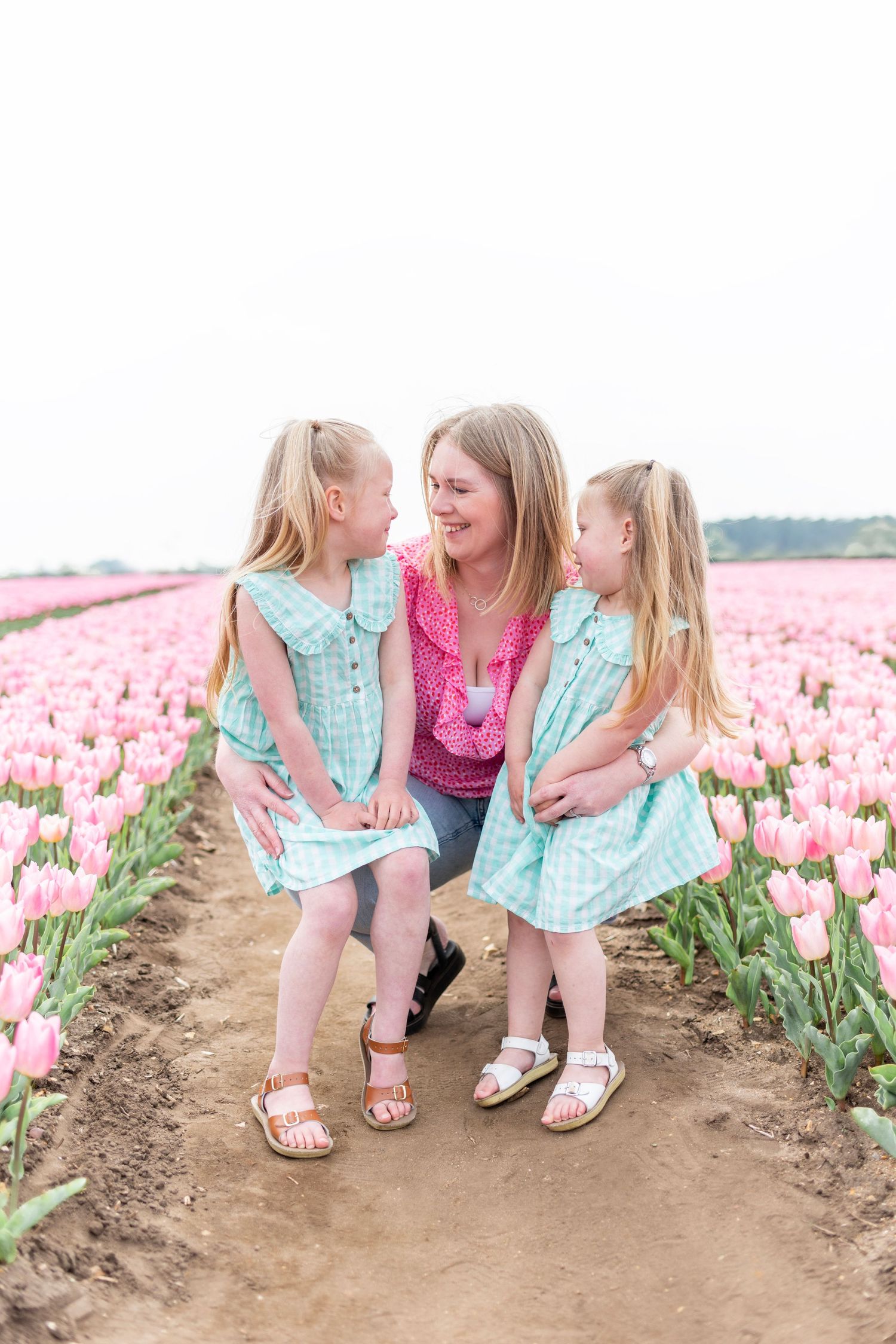 Mother and daughters in coordinating outfits sharing a moment among pink tulips.