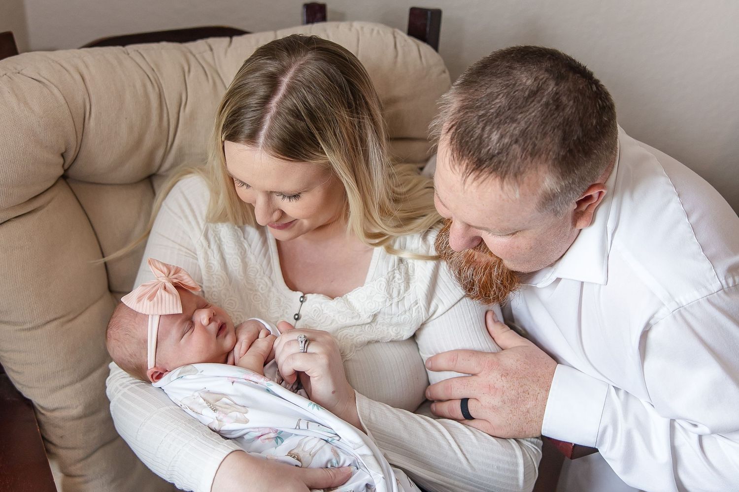New parents tenderly gaze at their newborn baby while sitting on beige couch.