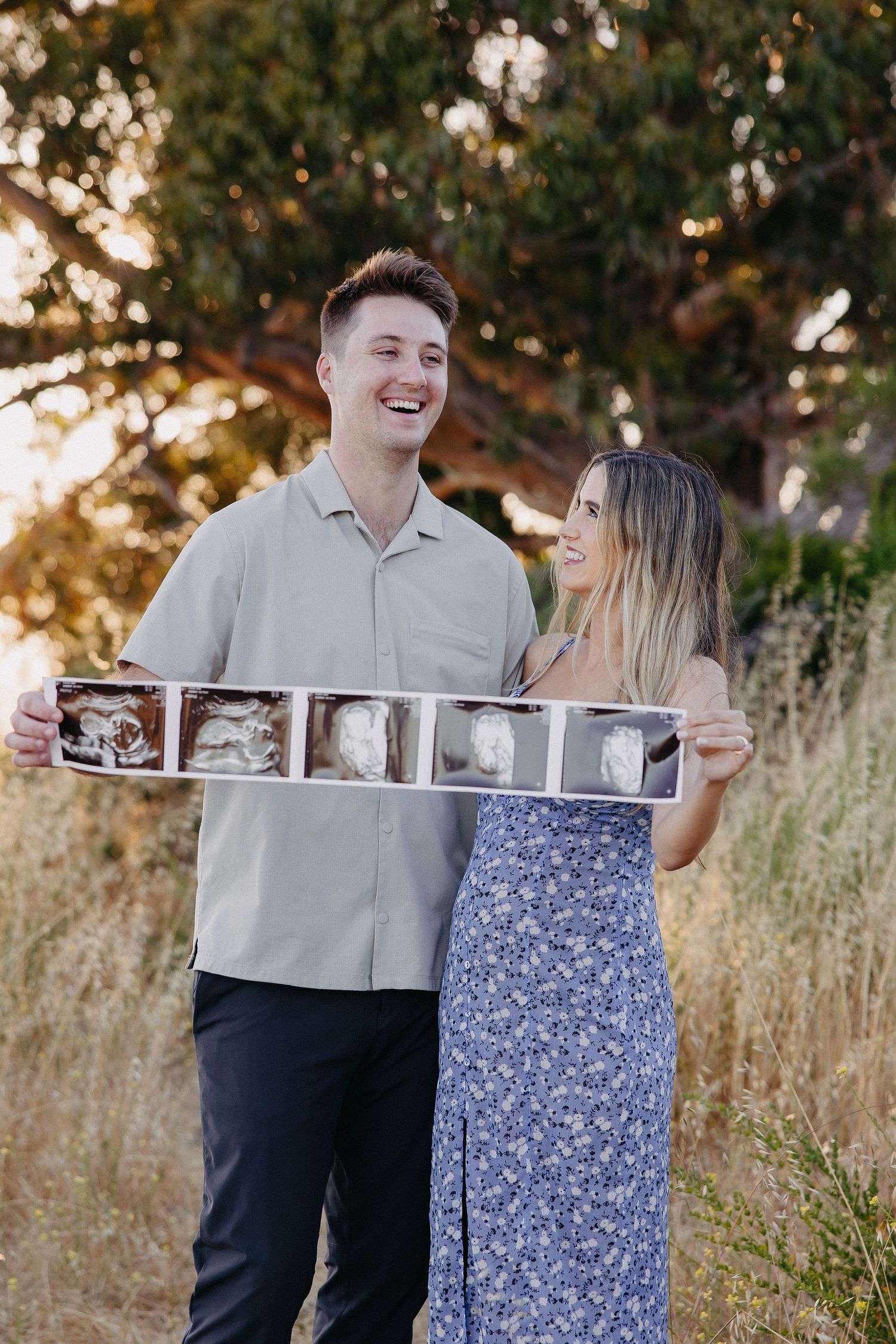 Happy couple outdoors sharing pregnancy news with ultrasound photo strip in golden hour light.