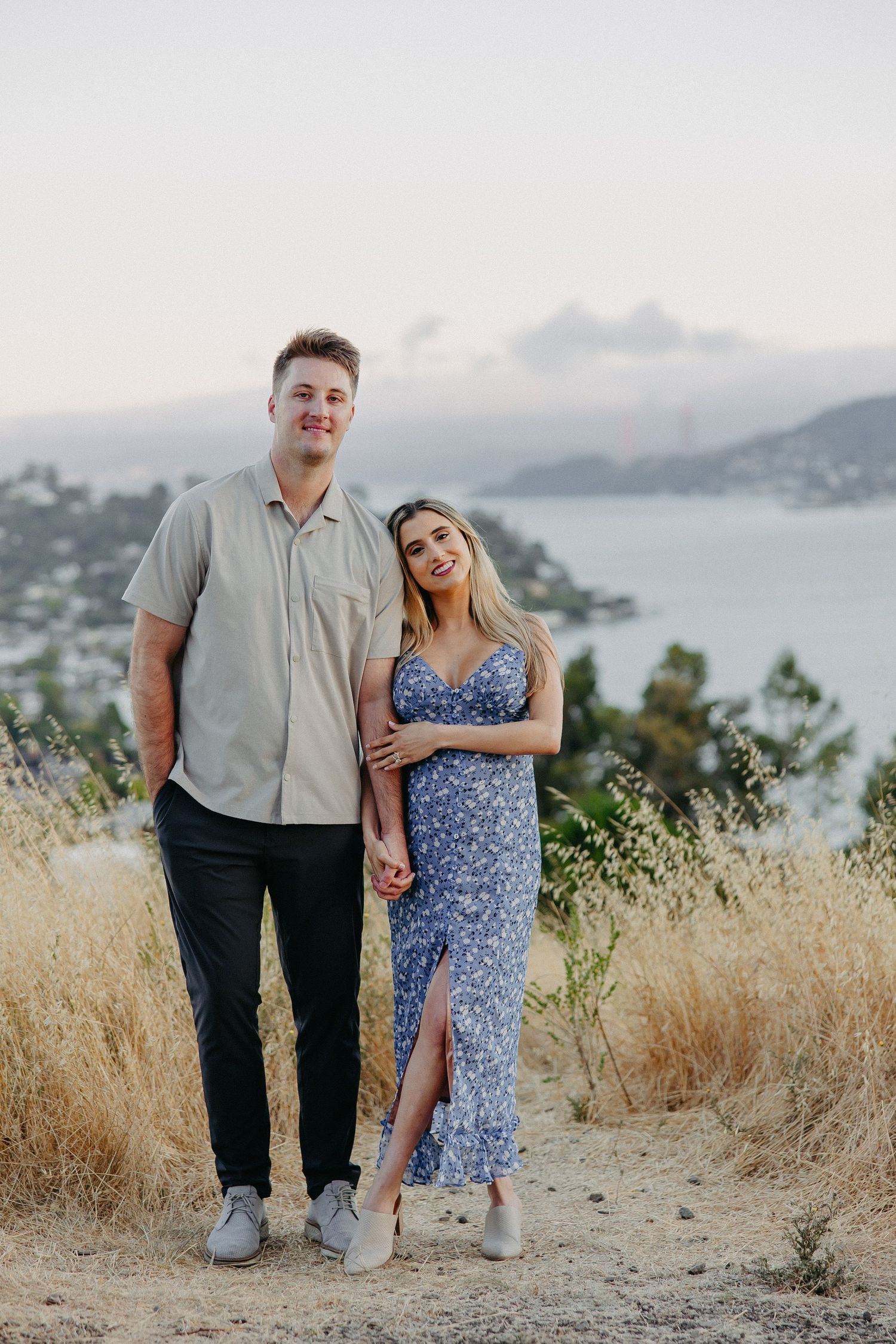 Couple standing together on trail with scenic bay view in background.