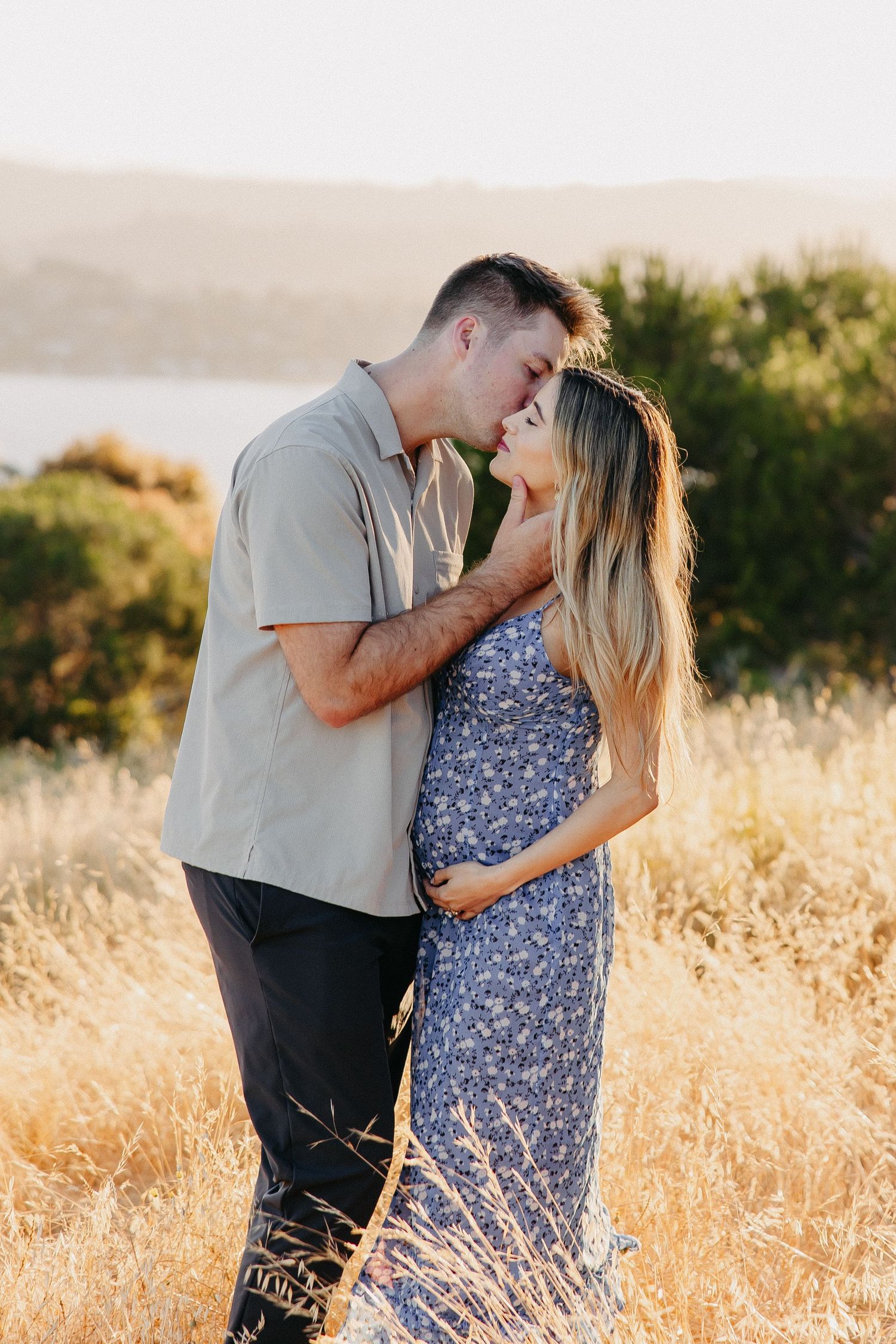 Intimate moment between couple standing in tall grass during golden hour.