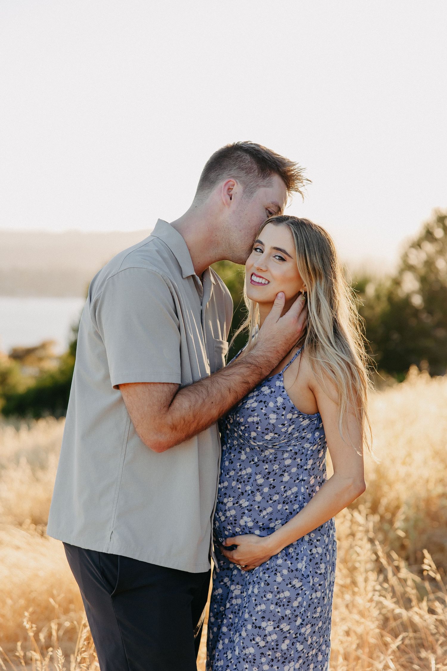 Romantic sunset portrait of couple in floral dress and grey shirt against nature backdrop.