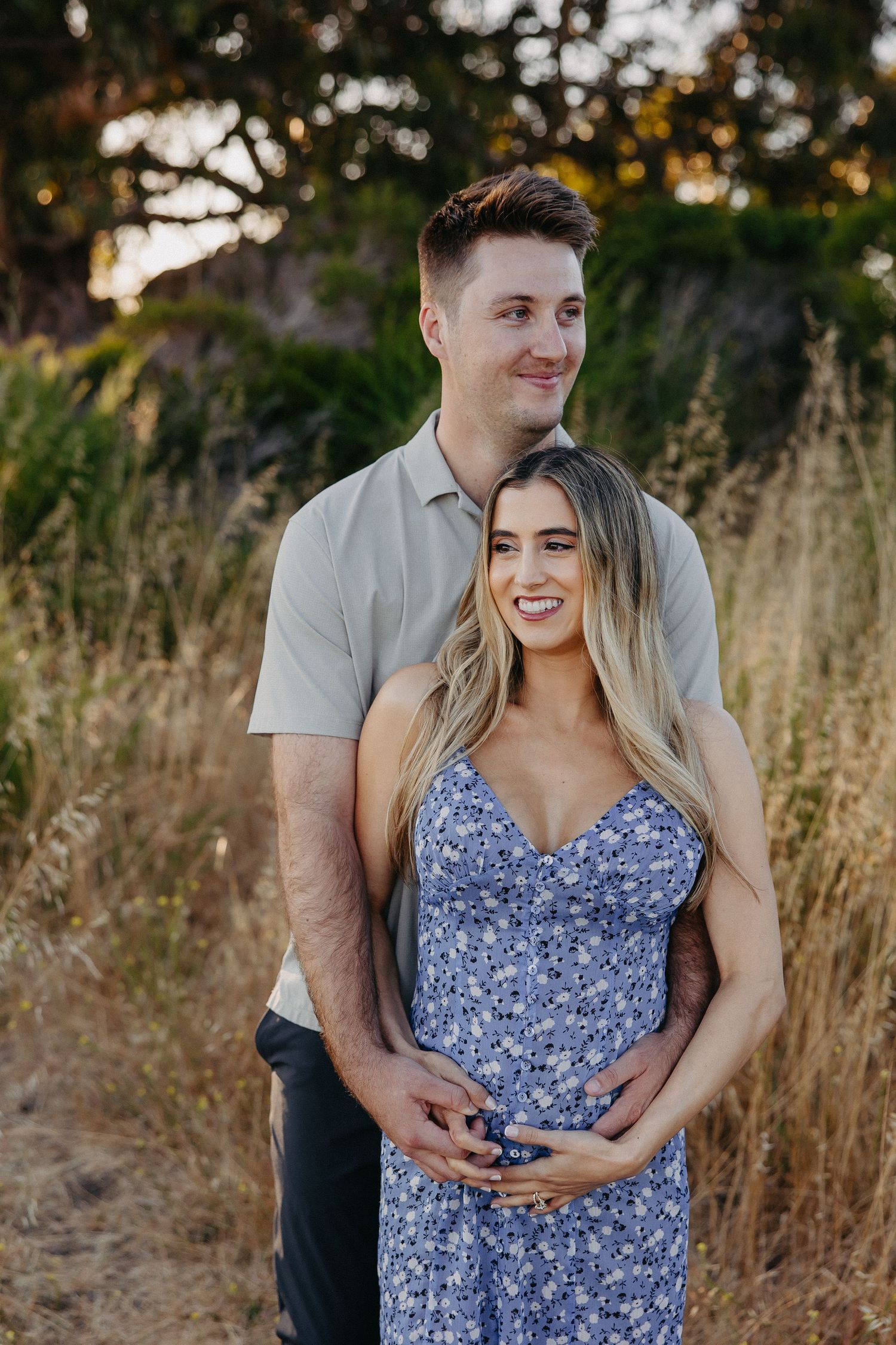 Happy couple embraces while posing for maternity photo in natural setting.