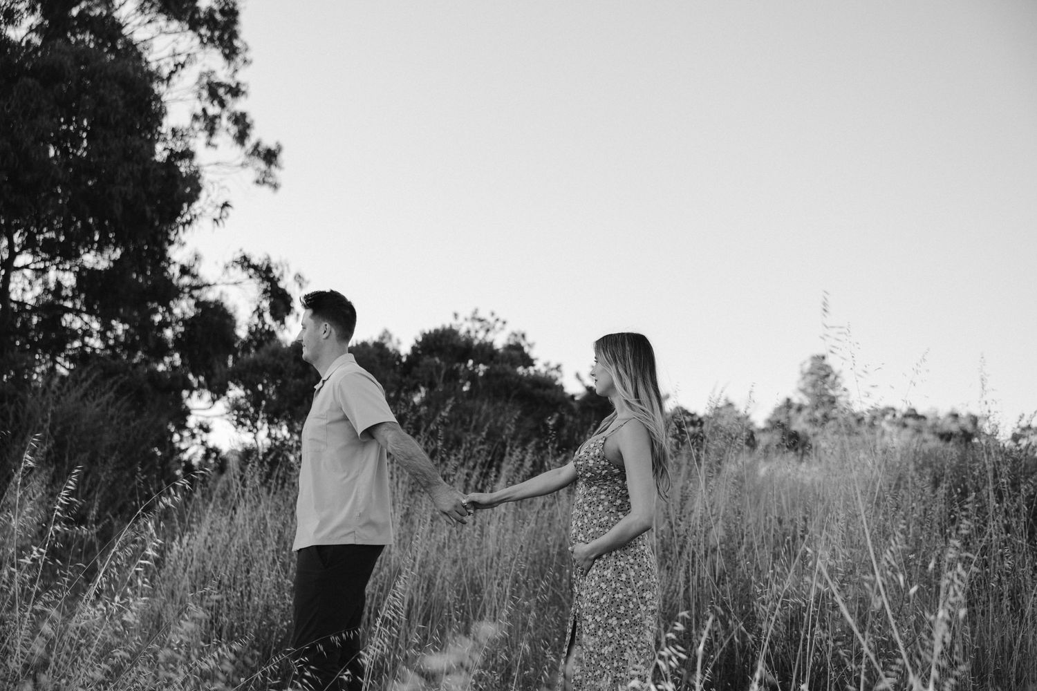 Black and white photo of a couple walking through tall grass in a field.