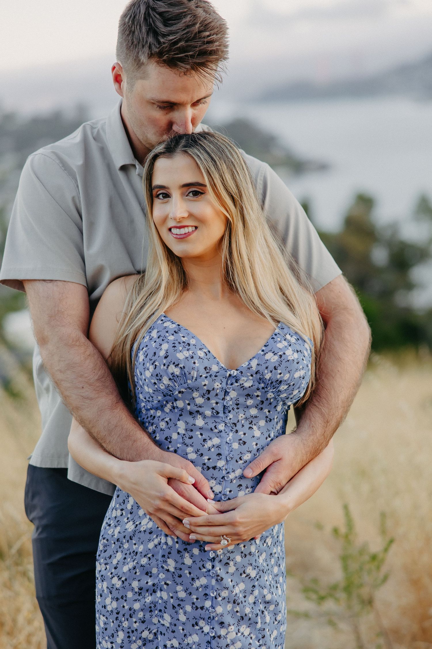Couple embracing in sunny field with blue floral dress and grey shirt.