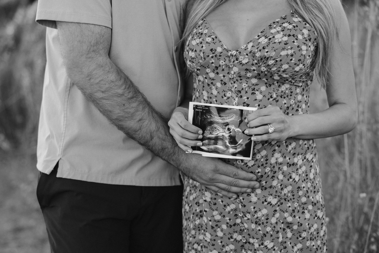 Black and white photo of couple holding ultrasound images in casual outdoor setting.