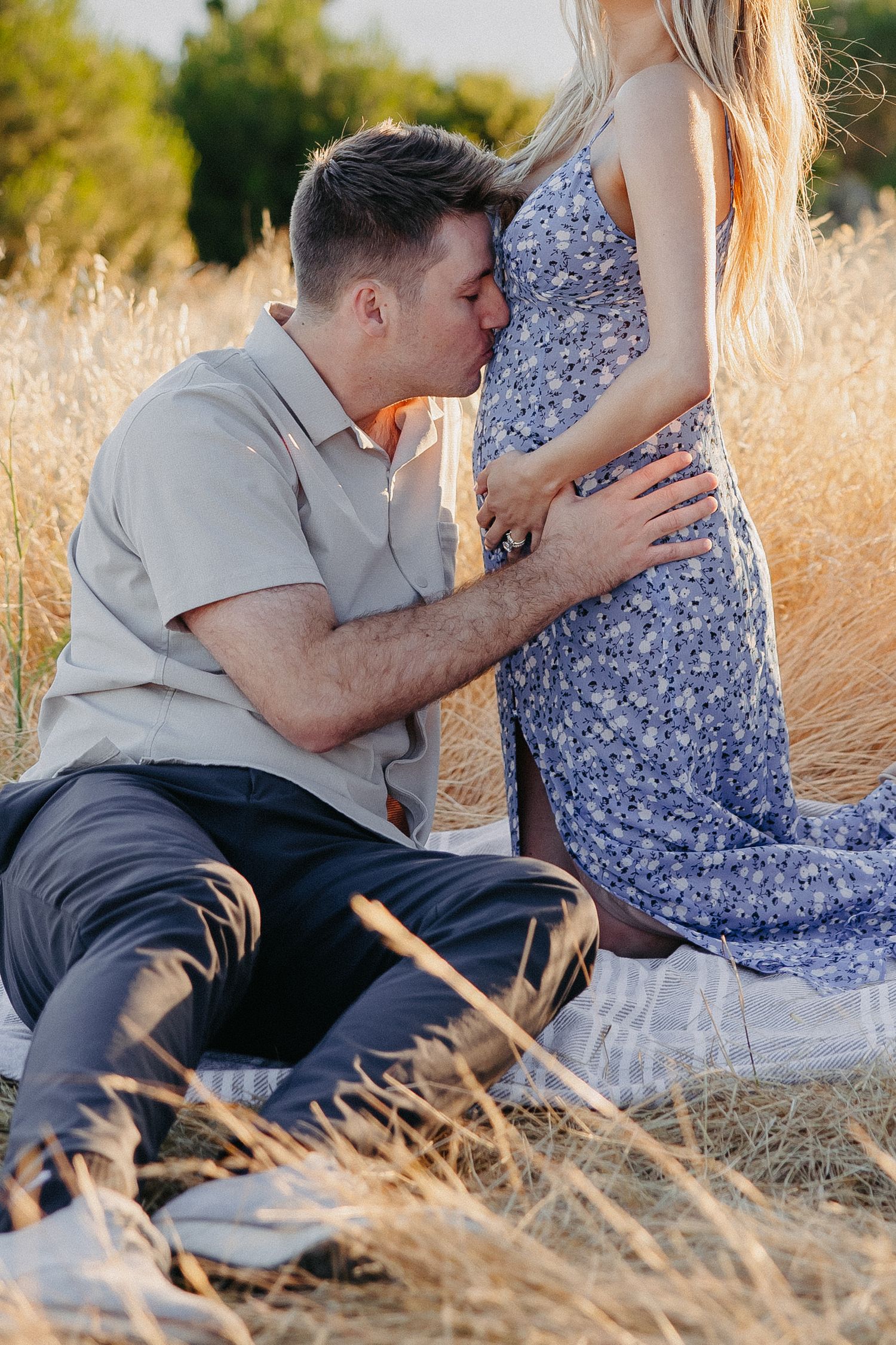Couple shares an intimate moment in a golden field overlooking a lake during sunset.