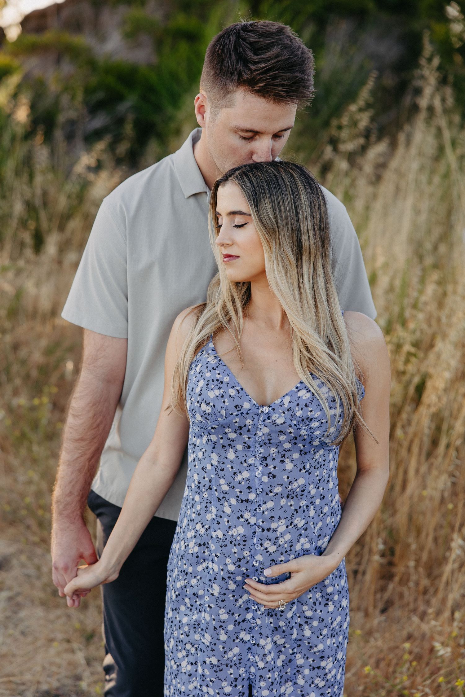 Intimate moment between couple in grey shirt and blue floral dress among tall grass.