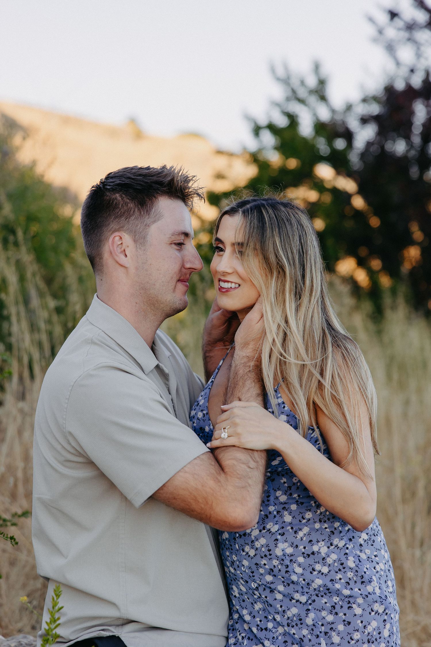Romantic couple shares intimate moment in field at sunset wearing coordinated blue and beige outfits.