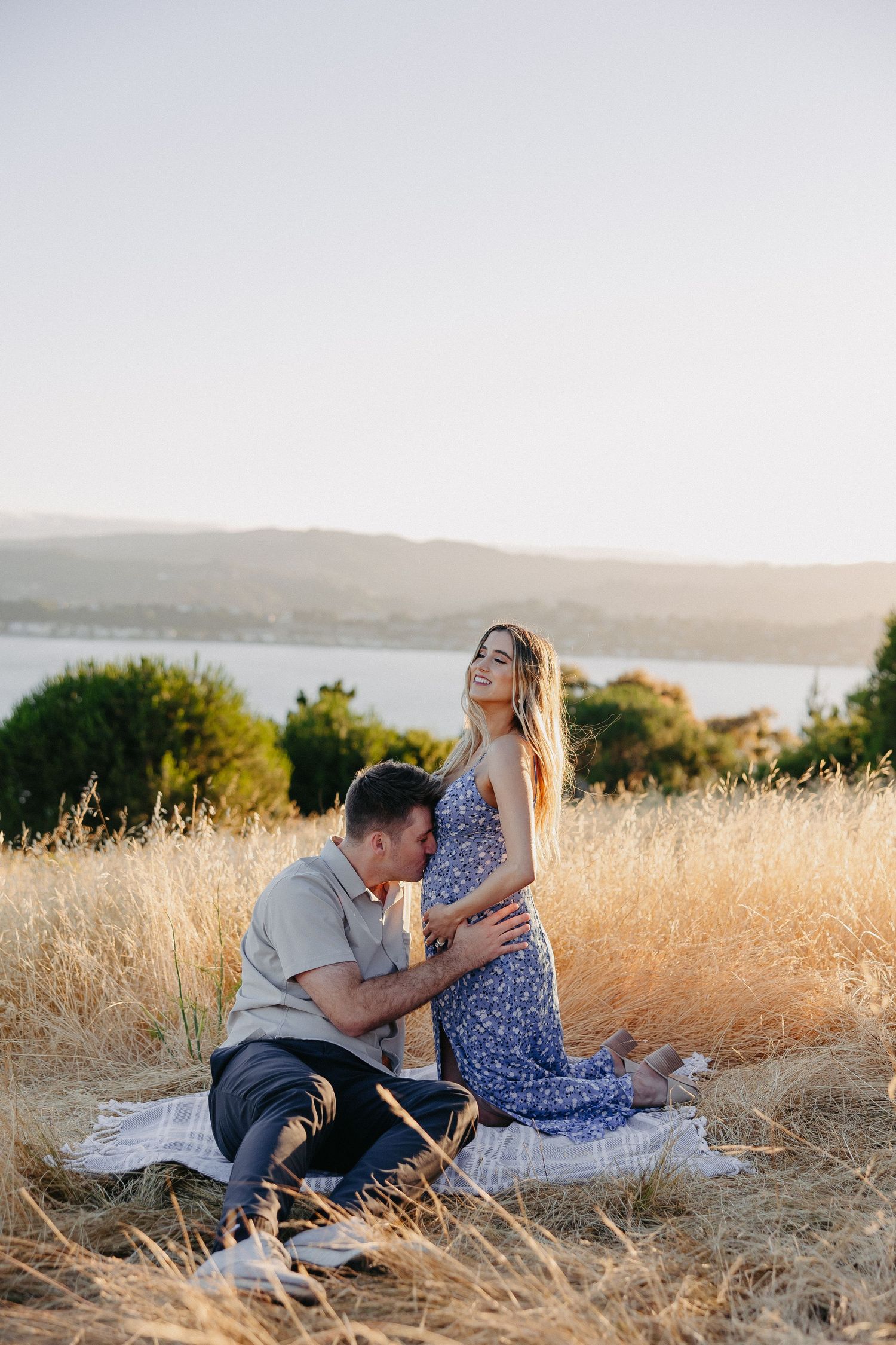 Sunset maternity photo session in golden field with couple on blanket.