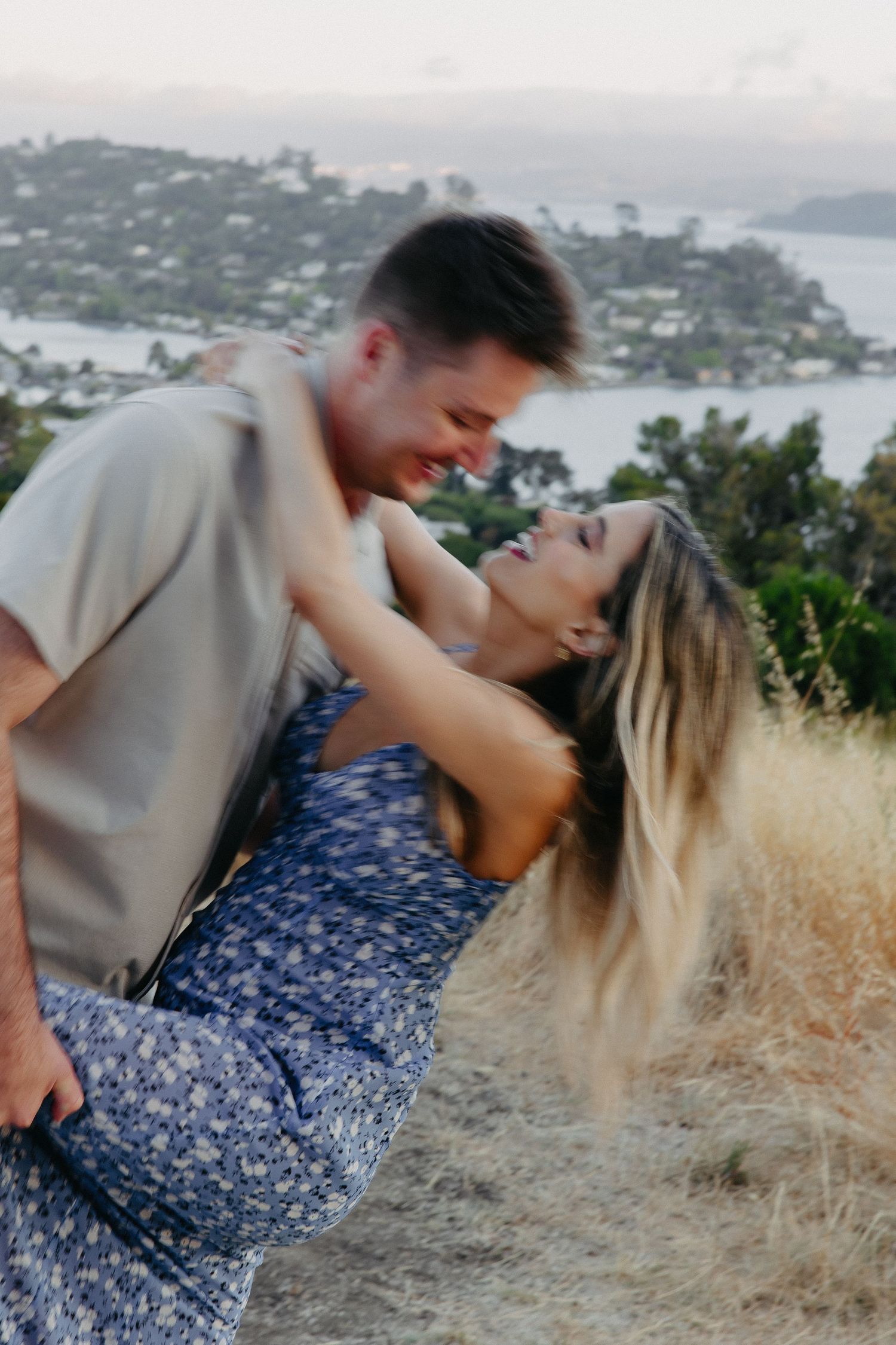 Joyful couple sharing playful moment on scenic hilltop during sunset photoshoot.