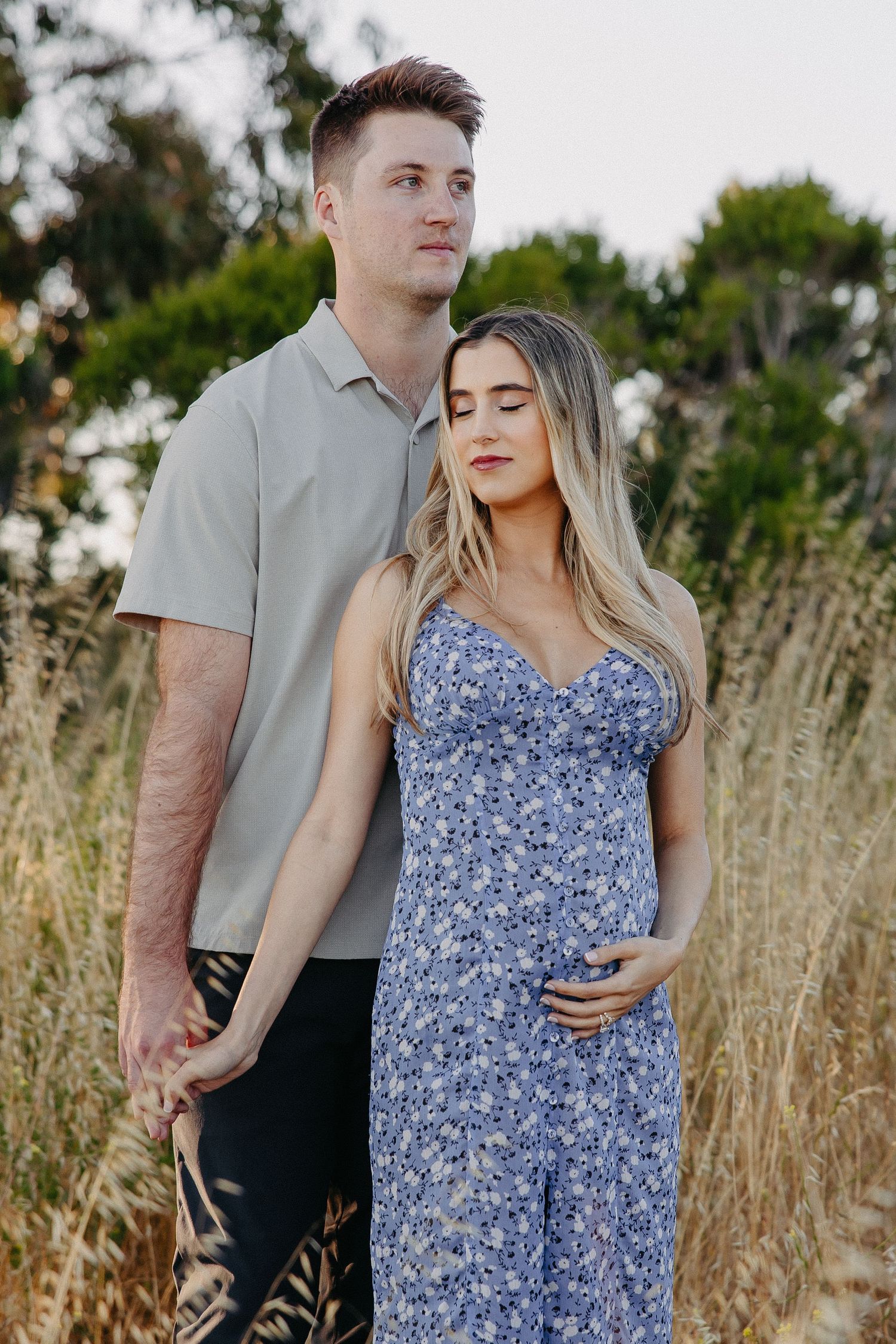 Intimate portrait of couple in grey shirt and blue floral dress against natural backdrop.