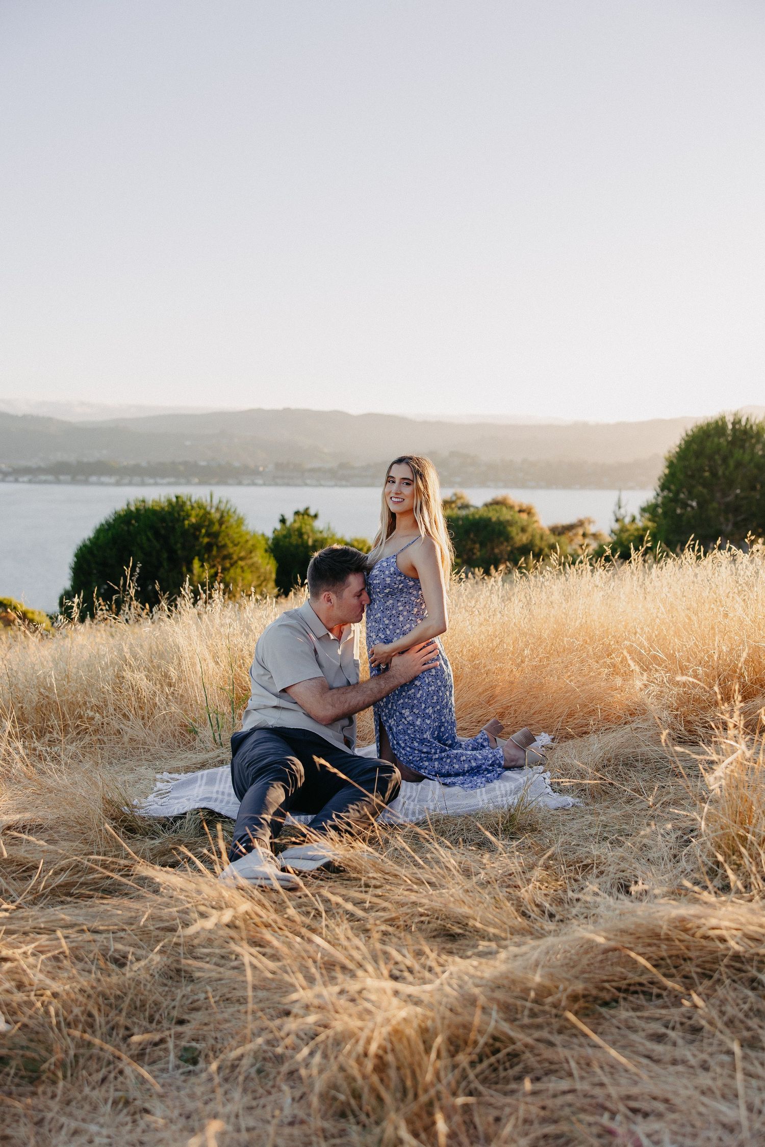 Couple sharing intimate moment on blanket in field during sunset.
