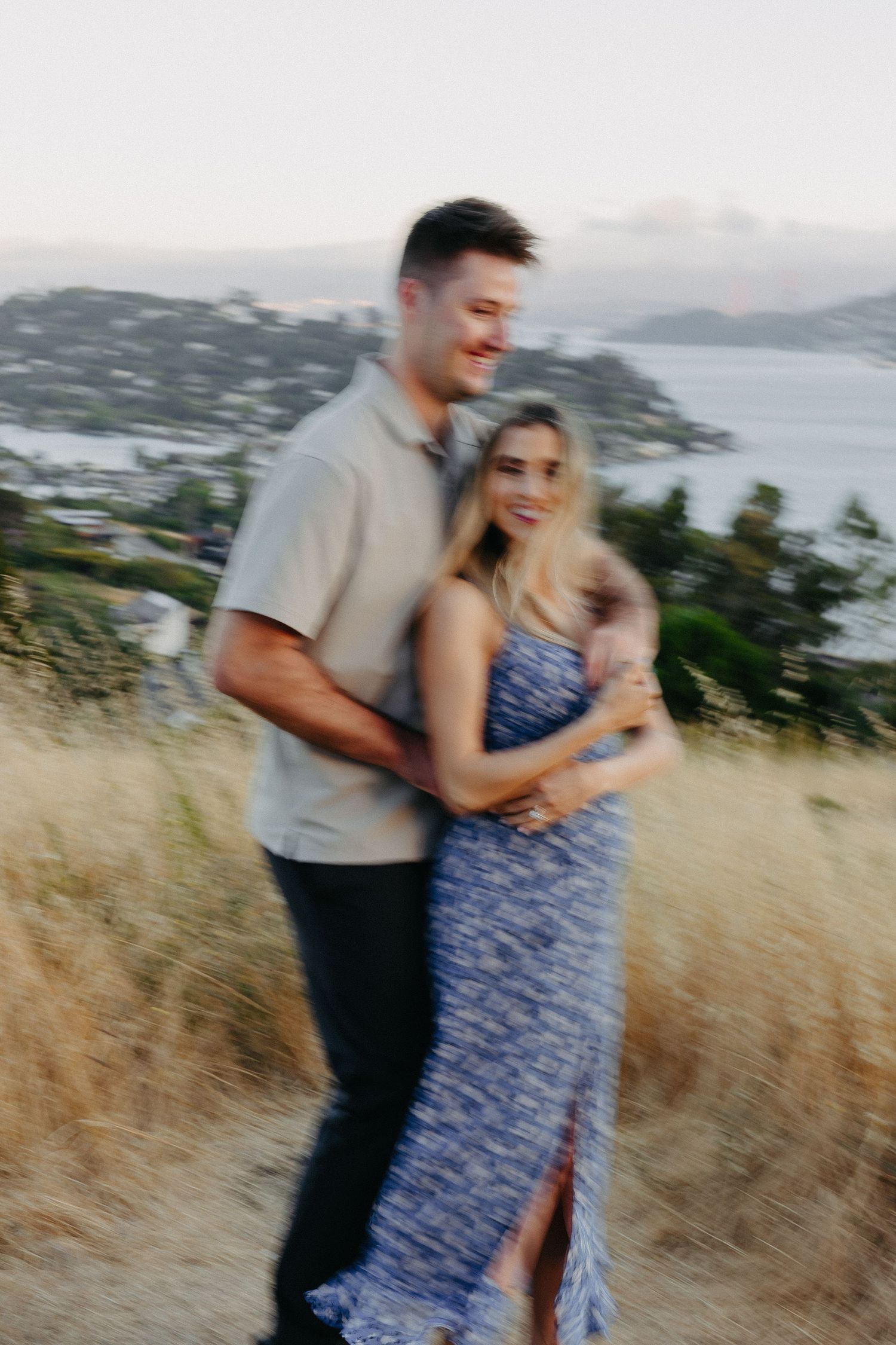 Romantic couple embracing on hilltop path with coastal view in background during golden hour.