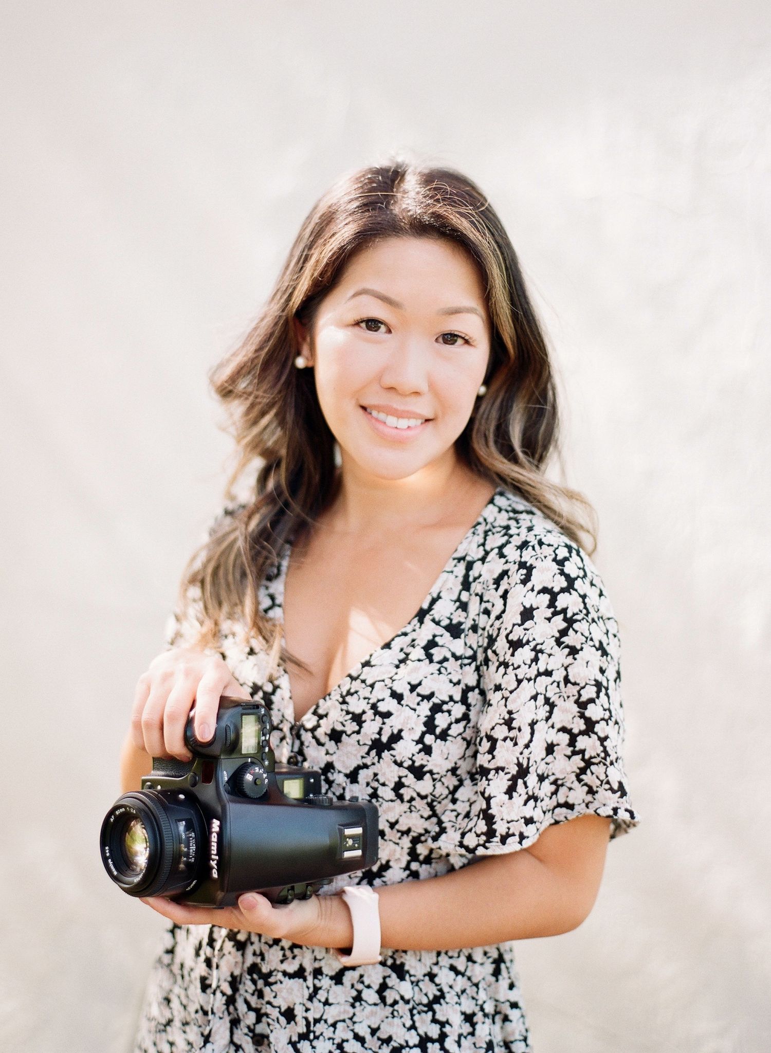 Portrait of photographer holding professional camera wearing floral print dress.