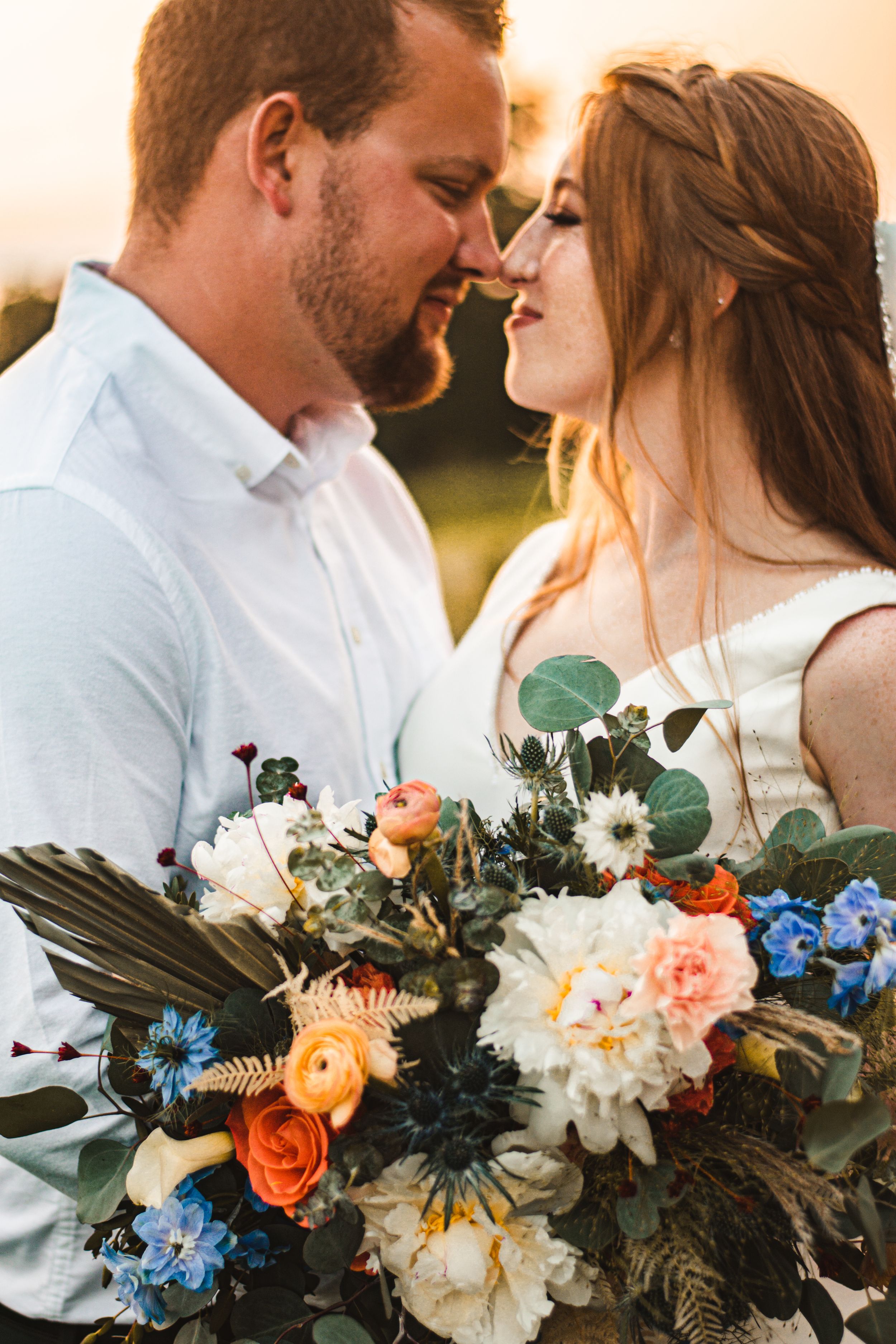 A tender moment between a couple with a stunning floral bouquet featuring roses and blue flowers.