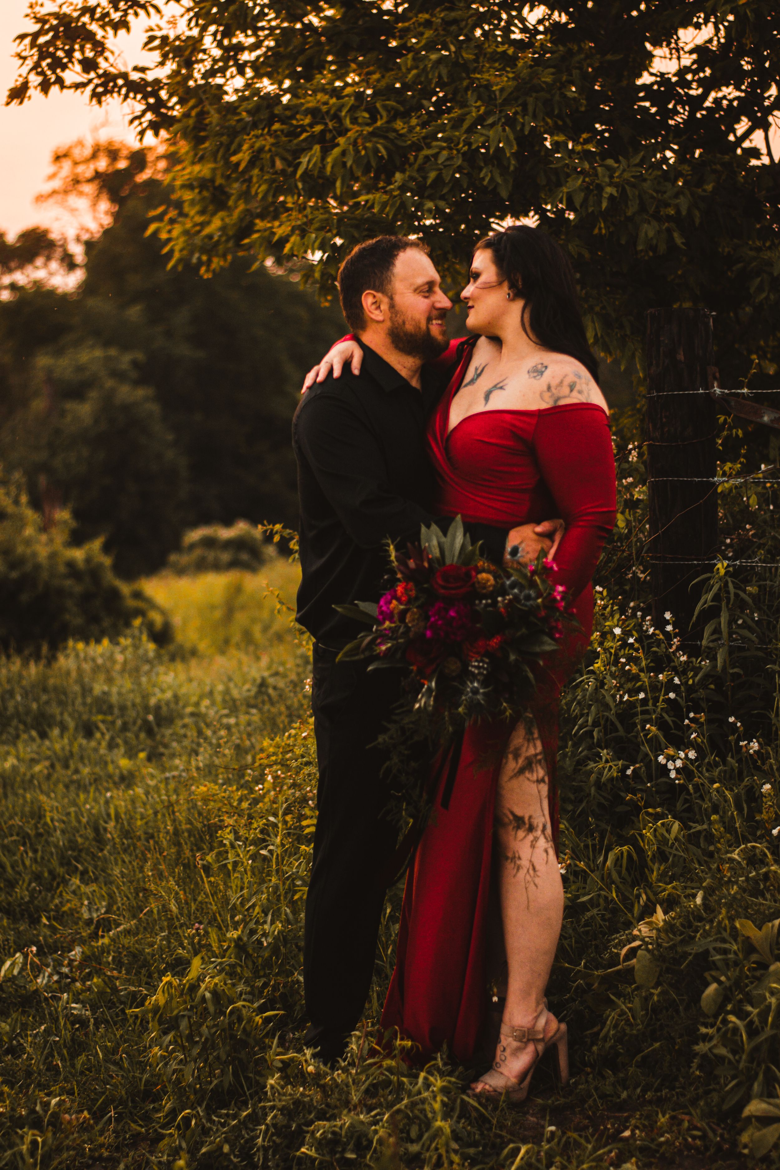 Romantic couple's portrait in nature with red dress and dramatic sunset lighting.