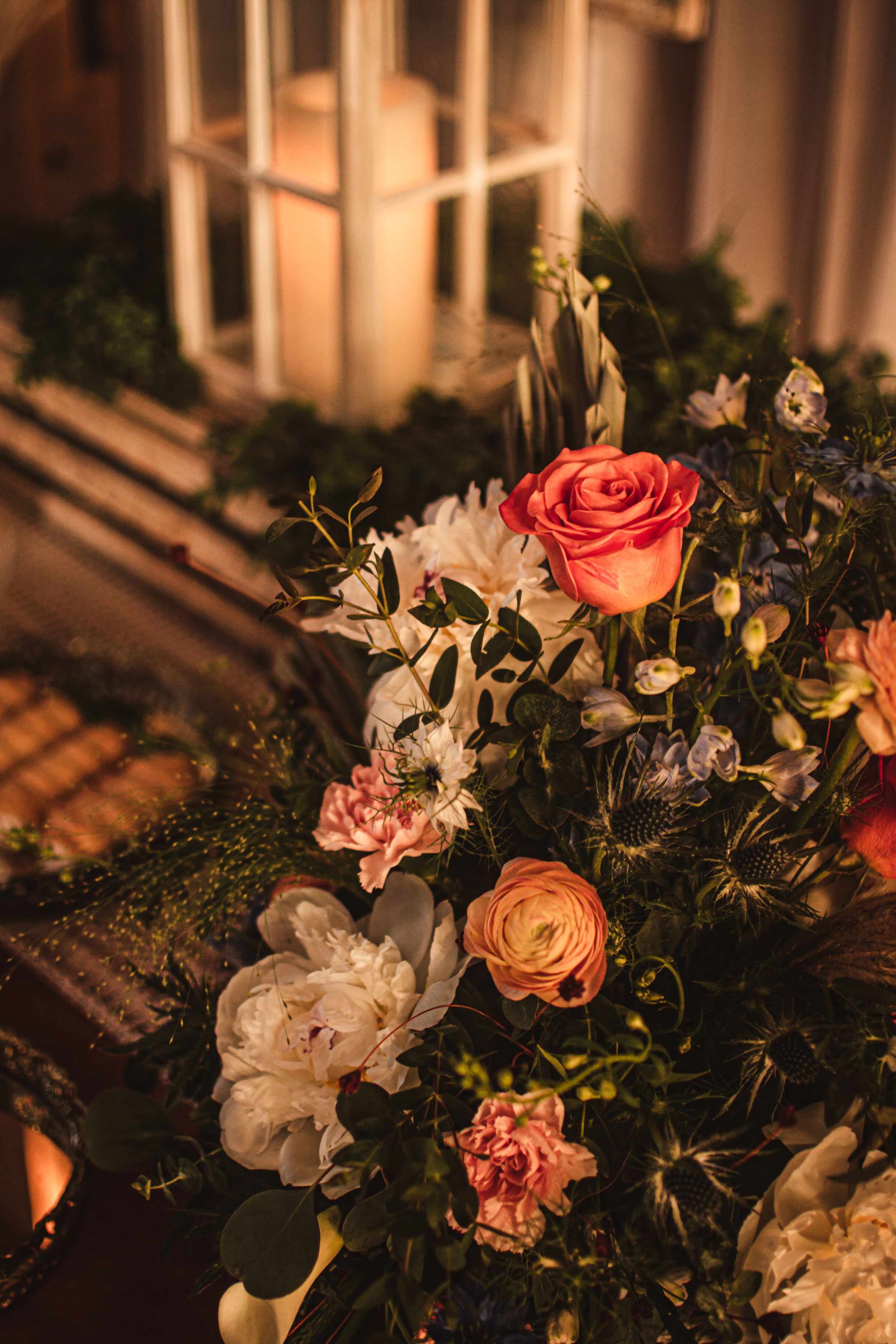 A beautiful floral arrangement with pink roses and white flowers sits by a window in warm lighting.