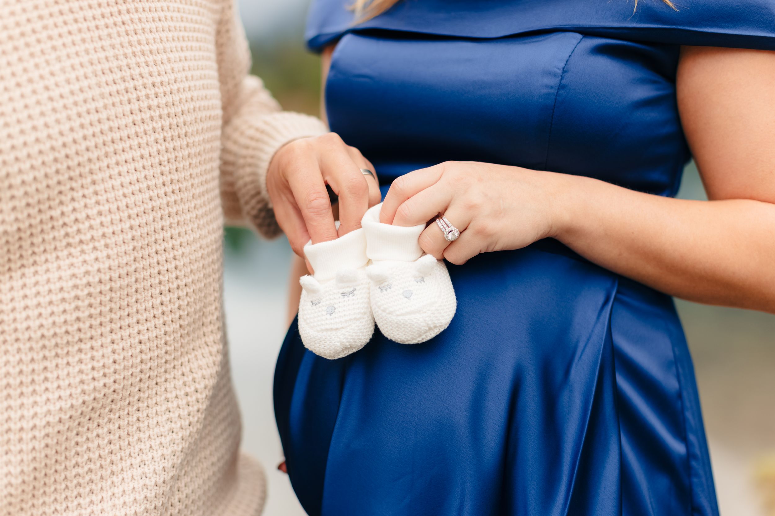 Hands hold tiny white baby shoes against a blue dress.