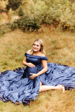 A woman in a navy blue dress sits gracefully in a grassy field.
