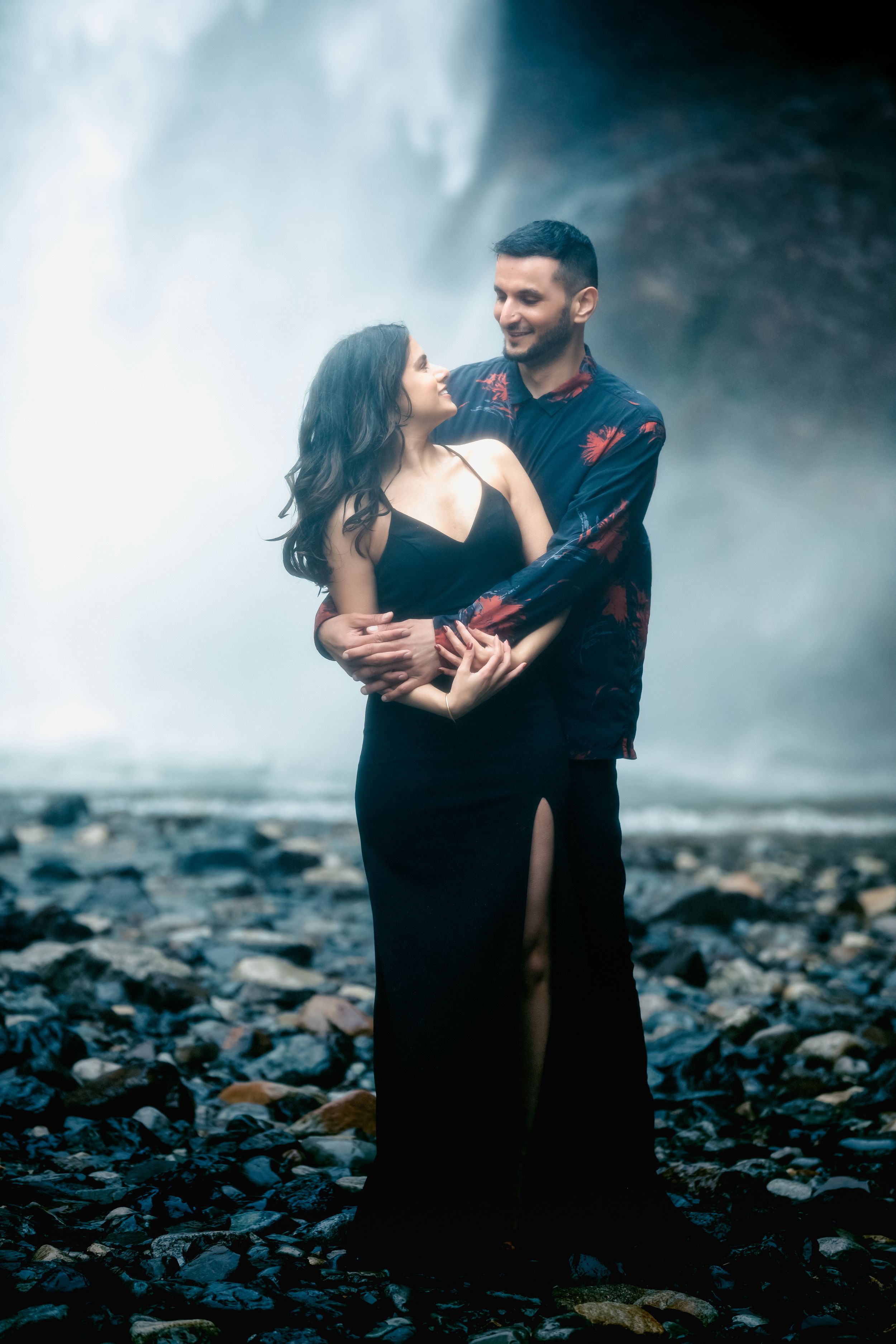 A romantic couple poses against the misty backdrop of a waterfall.