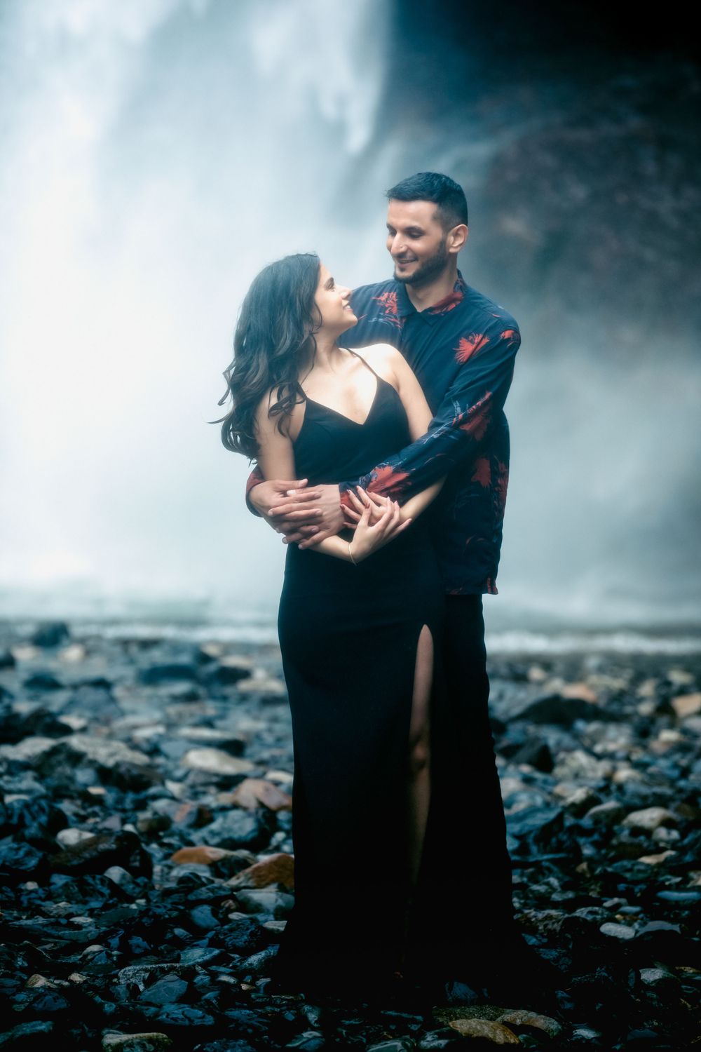 A romantic couple poses against the misty backdrop of a waterfall.