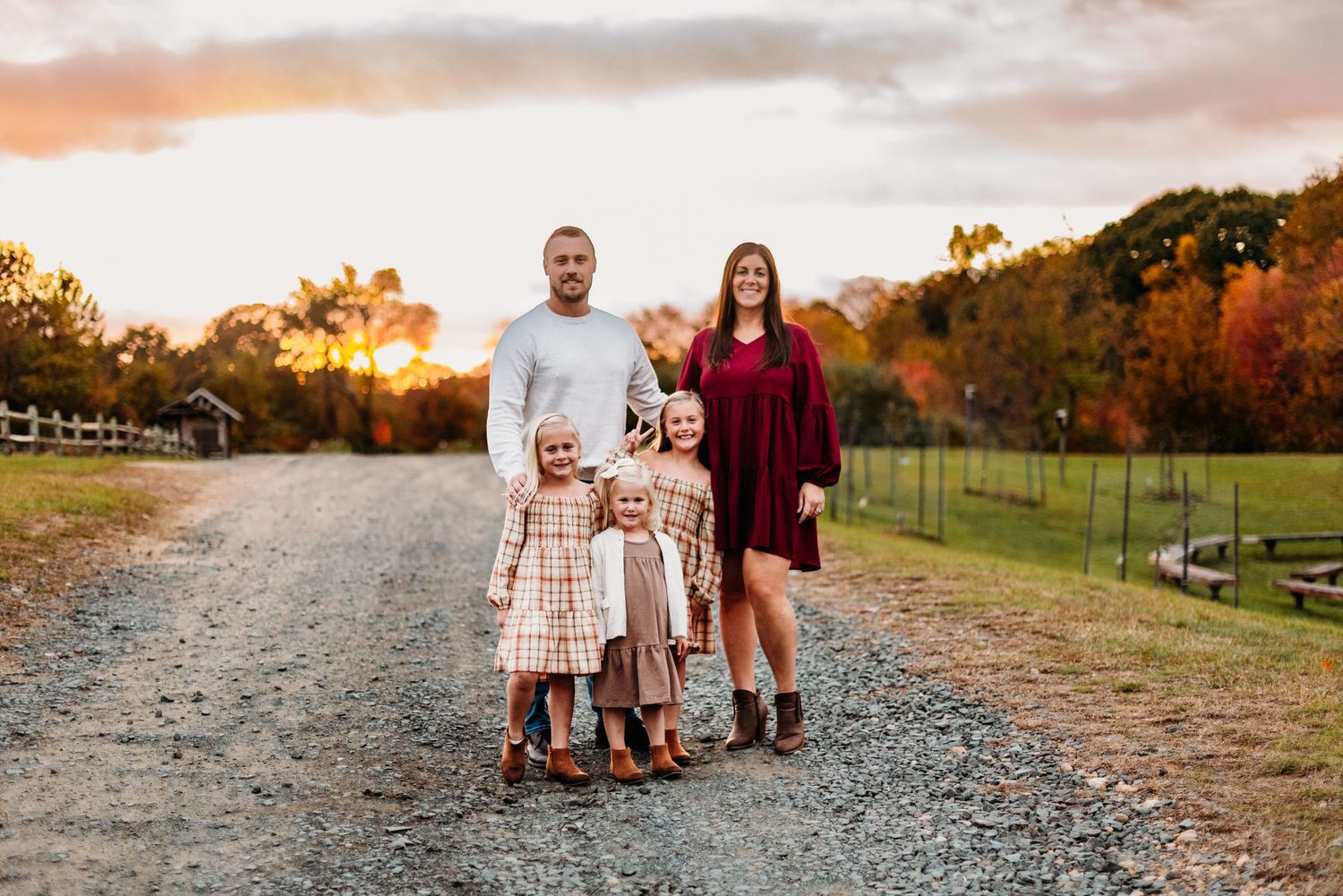 Family of four poses together on gravel path during golden hour in autumn setting.